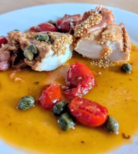 Sliced chicken breast topped with mustard caviar in a golden cherry-tomato and caper pan sauce.