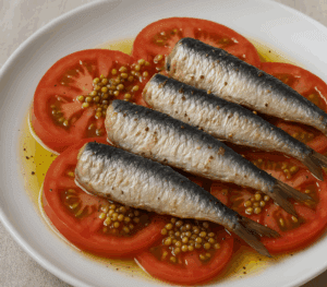 Plate of Albatros sardines in olive oil served on sliced Cuore di Bue tomatoes with mustard caviar and EVOO drizzle – a Mediterranean longevity meal.